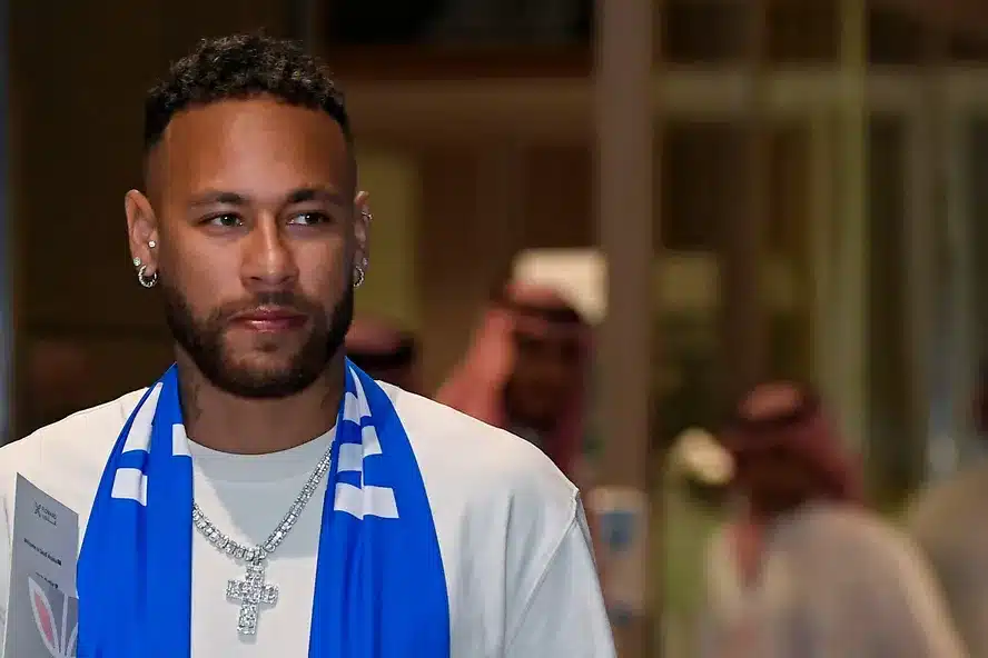 Neymar sorridente em sua apresentação no Al-Hilal, cercado por membros do clube e jornalistas.