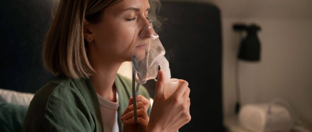 Mulher usando um nebulizador em ambiente doméstico, respirando profundamente com olhos fechados.
