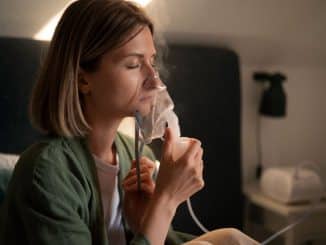 Mulher usando um nebulizador em ambiente doméstico, respirando profundamente com olhos fechados.