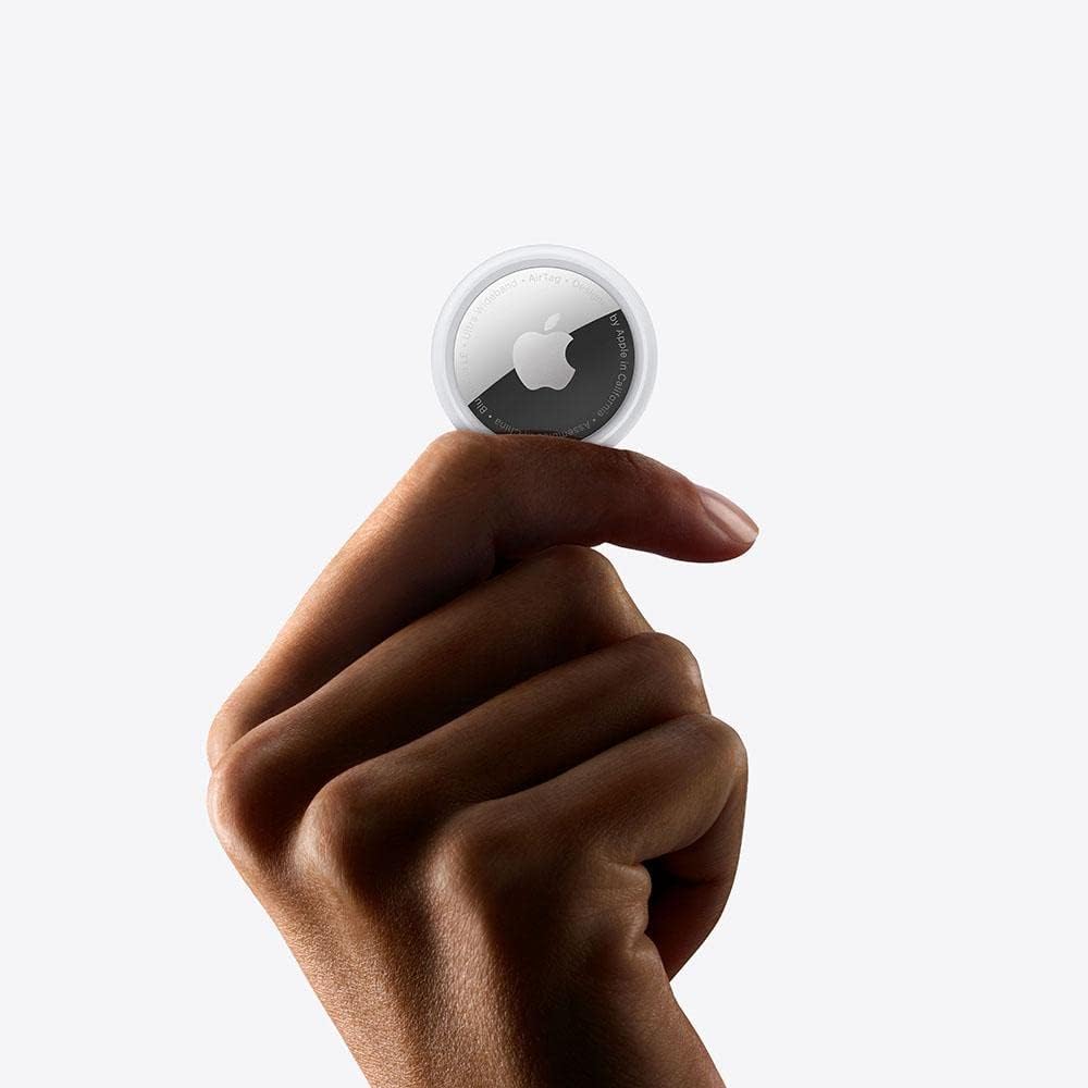 Imagem de uma mão segurando um AirTag da Apple, destacando seu design elegante e a logomarca da Apple.