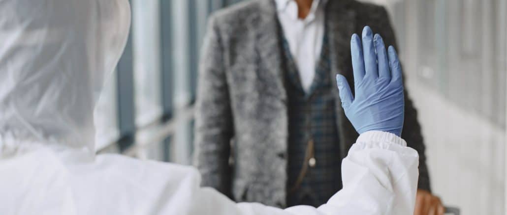 Um profissional de saúde em traje de proteção completa levanta a mão em sinal de parada para um homem de negócios usando máscara.
