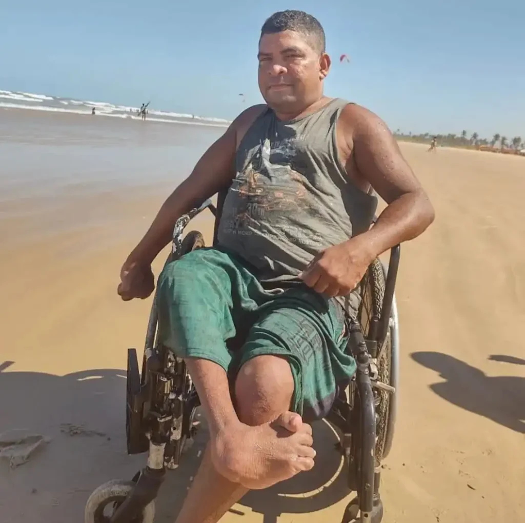Silvaneto Santos, em sua cadeira de rodas, contempla a praia em um dia ensolarado.