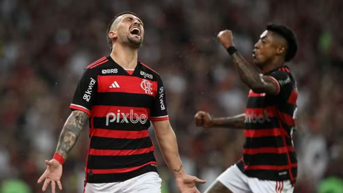 Jogador do Flamengo, Giorgian De Arrascaeta, comemora efusivamente após marcar o gol da vitória contra o Bahia, enquanto Bruno Henrique ergue o punho em celebração.