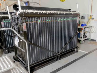 Estrutura industrial de bateria de ferro com múltiplas placas verticais pretas e conexões em ambiente de tecnologia.