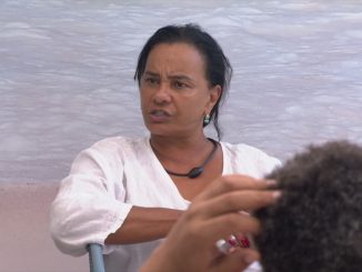 Solange Couto de blusa branca e colar preto com expressão séria conversando com outra pessoa.