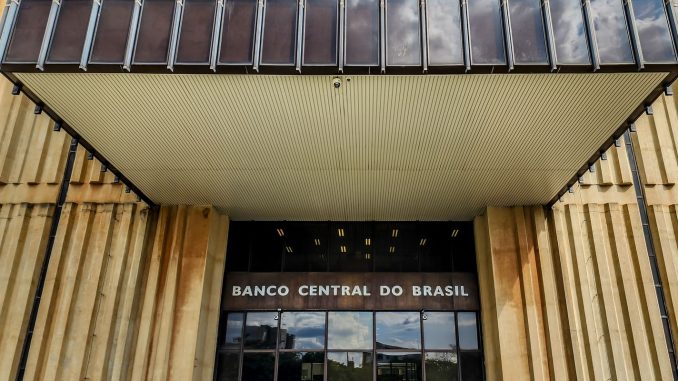 Vista externa do edifício-sede do Banco Central do Brasil, uma estrutura arquitetônica moderna com janelas escuras sob um céu claro.