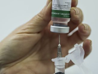 Profissional de saúde aplica vacina no braço de um paciente em unidade de saúde.