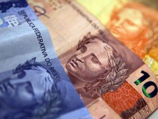Cédulas de Real e moedas brasileiras sobrepostas em uma superfície.