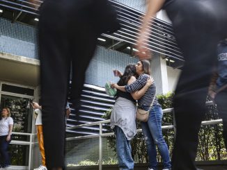 Estudantes em uma sala de aula realizando uma prova, focando em cadernos de questões e canetas.