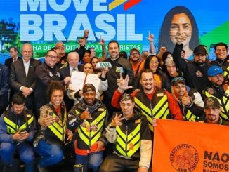 Presidente Lula assinando documento durante evento em São Paulo cercado por autoridades e representantes de motoristas.
