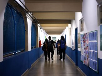 Vista do pátio de uma escola pública com alunos ao fundo.